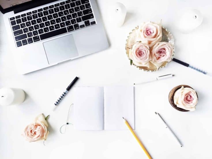 feminine laptop desktop with pale roses and notebooks scattered around, Workspace with pen, pencil, laptop, pink rose flower, golden vintage tray, candle on white background. Flat lay, top view